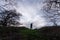 A spooky, hooded figure standing on a country path between trees on a winters day