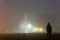 A spooky hooded figure standing in front of a church lit up on an atmospheric foggy, winters night