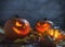 Spooky pumpkins jack o lantern among dried leaves on wooden fence