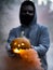 Spooky shot of a European guy holding a smoking Halloween pumpkin while wearing a facemask