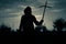 A spooky silhouette of a hooded man standing outside holding a wooden homemade cross at sunset. With a vintage grainy edit