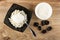 Spoon in black bowl with grainy cottage cheese and sour cream, bowl with sour cream, prunes on wooden table. Top view