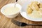 Spoon in bowl with condensed milk, dumplings with cottage cheese filling, condensed milk in plate, fork on wooden table