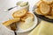 Spoon in bowl with condensed milk, pancake on fork, pancake with condensed milk in saucer, plate with pancakes, napkin on wooden