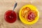 Spoon in bowl with jam, cheese pancakes with jam in saucer on table. Top view