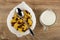 Spoon in bowl with raisin and corn flakes, pitcher with yogurt on table. Top view