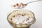 Spoon with breakfast cereals and yogurt above brown bowl