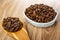 Spoon with coffee beans, blue bowl with roasted coffee beans on wooden table