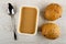 Spoon, container with peanut butter, buns on wooden table. Top view