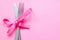 Spoon with a fork tied with a ribbon on a pink background. Cutlery