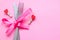 Spoon with a fork tied with a ribbon on a pink background. Cutlery