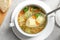 Spoon of fresh homemade vegetable soup over full dish on light grey table