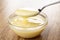 Spoon with milk above transparent bowl with condensed milk on table