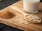 Spoon of oat-flakes, a glass of milk, and crumbs on a wooden board