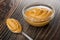 Spoon with peanut butter, transparent bowl with peanut butter on wooden table