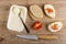 Spoon in plastic jar with creamy cheese, pieces of bread, sandwiches with cheese, tomato and dill, knife on table. Top view