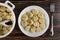 Spoon in plastic pan with boiled dumplings, plate with dumplings, fork on wooden table. Top view