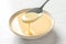 Spoon with pouring condensed milk over bowl on white, closeup. Dairy products