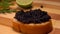 Spoon is pressing black caviar to the piece of bread on the background of lime