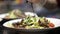 Spoon with sauce is poured over salad. Action. Closeup of aesthetic pouring jets of salad sauce by professional chef in