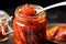 a spoon scooping vibrant red kimchi from a glass jar