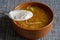 A spoon with sour cream and cabbage soup in a brown earthenware bowl on a blue tablecloth