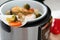 Spoon with steamed garnish and blurred multi cooker on background. Space for