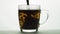 Spoon stirs tea in transparent glass cup creating whirl, black particles spinning brewing tea. slow motion isolated on