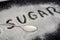Spoon with sugar, the inscription `sugar` on white sugar. Sugar on a black background. Disease Warning.