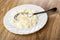 Spoon in white plate with cottage cheese poured condensed milk on wooden table