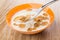 Spoon with yogurt, multicereal flakes above bowl on table