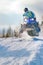 Sport blue snowmobile jump. Cloud of snow dust from under snowmobile tracks. Front view, vertical shot.