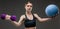 Sport caucasian girl with slim figure do exercises with blue ball and purple dumddell isolated on black background