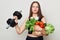 Sport and healthy eating. Sad unhappy woman lifting holding barbel and fresh vegetables isolated over white background looking at