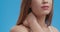 Sport injury. Young female massaging her inflamed neck muscles, close up shot, blue studio background