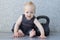 Sport is life. Happy smiling toddler sitting on the floor with kettlebell.
