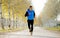 Sport man running outdoors in off road trail ground with trees under beautiful Autumn sunlight