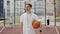 Sport school trainer standing on playground and holding a ball. Man with moustache turn head looking at camera. People