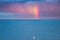 Sport, travel and leisure: A lonely sailing boat in Dublin bay on the Atlantic Ocean at dusk with a rainbow on the horizon