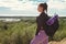 Sporting woman single tourist with backpack and rug stands on hill above the forest and looks to the side