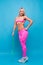 Sportive blonde girl in the pink sportswear with skipping rope on the blue background in the studio