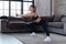 Sportive Caucasian female athlete in black sports bra and leggings doing side squat exercise at home