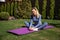 Sportive fitness woman sitting on pink mat at the garden