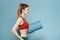 Sportive woman training mat in hands Red tank top exercise blue background