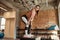 Sportive young woman looking aside, standing on plyo box while having workout at industrial gym