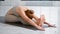 Sportive young woman yoga trainer in stylish beige top does head to knees exercise on parquet floor in light studio