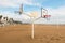 Sports area on the sand of the beach without people, with volleyball net and triple basketball basket in the foreground