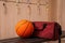 Sports bag and basketball ball on wooden bench in locker room