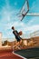 Sports and basketball. A young teenager in a blue tracksuit throws a ball into the basket in a powerful jump. Blue sky in the