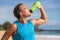 Sports bottle drink sport man drinking water on beach run. Male runner sweaty and thirsty after difficult workout